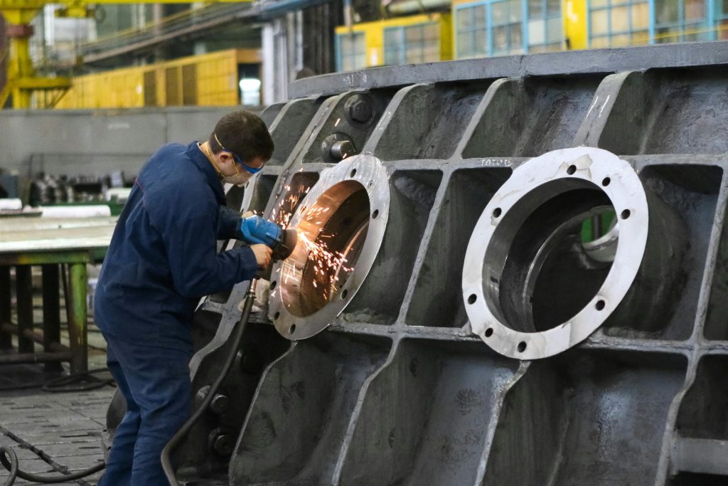 Ein Arbeiter in Schutzkleidung schleift in einer Fabrik Metall und erzeugt dabei Funken.